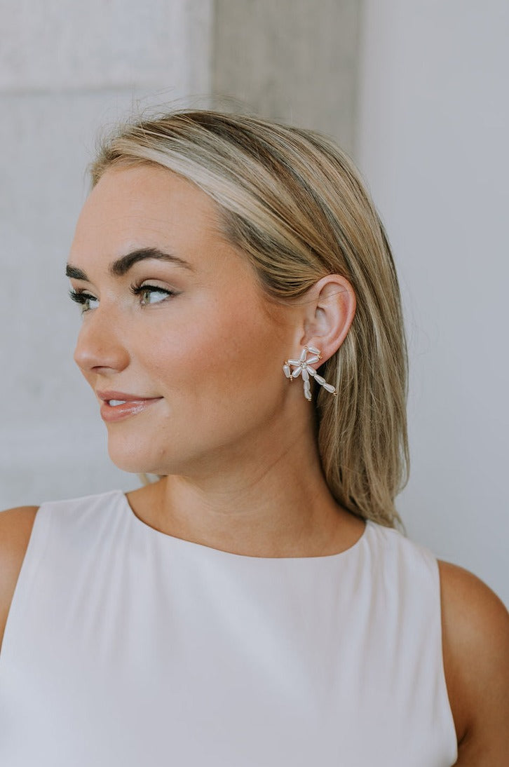 Side view of female model wearing the Yara Beaded Bow Earrings that have white and gold beads in the shape of a bow.