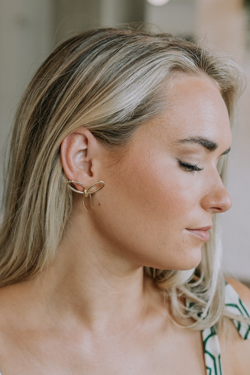 Side view of female model wearing the Charlie Gold Bow Shaped Stud Earring which features gold bow shaped studs