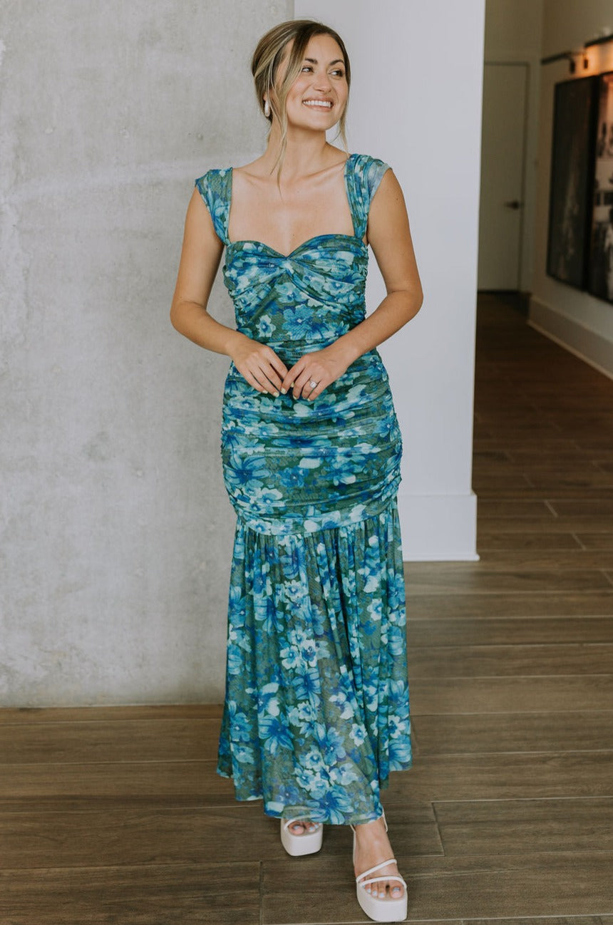 Full body view of female model wearing the Khloe Blue & Green Floral Ruched Midi Dress which features Blue and Green Floral Print, Ruched Fabric, Flare Skirt Hem with Slit, Sweetheart Neckline, Straps and Monochrome Side Zipper with Hook Closure