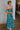 Full body side view of female model wearing the Khloe Blue & Green Floral Ruched Midi Dress which features Blue and Green Floral Print, Ruched Fabric, Flare Skirt Hem with Slit, Sweetheart Neckline, Straps and Monochrome Side Zipper with Hook Closure