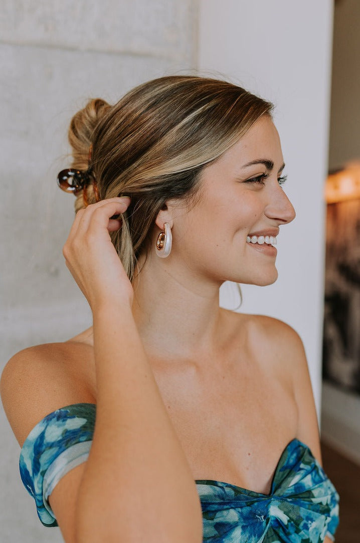 Side view of female model wearing Faye White & Gold Teardrop Hoops that have pearlescent white teardrop-shaped hoops with gold trim