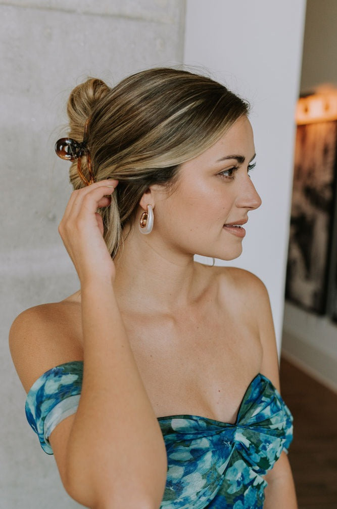 Side view of female model wearing Faye White & Gold Teardrop Hoops that have pearlescent white teardrop-shaped hoops with gold trim