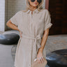 Upper body front view of female model wearing the Valentina Taupe & Cream Striped Romper that has cream and taupe vertical stripes, a button up front with a collar, a tie belt, and short sleeves.