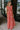 Full body side view of female model wearing the Adalyn Pink & Red Paisley Cut-Out Maxi Dress which features Red, Pink and Peach Paisley Print, Side Ruffle Slits, Peach Thigh Length Lining, Maxi Length, Elastic Waistband, Side Cutouts with Rattan Buckle, Plunge Neckline, Ruffle Straps andTie Back Closure