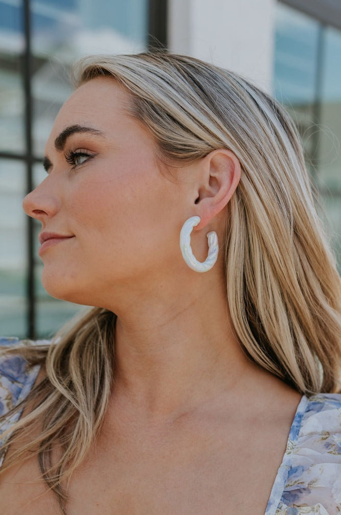 Side view of female model wearing the Myra Iridescent Hoop Earrings that have white iridescent material.