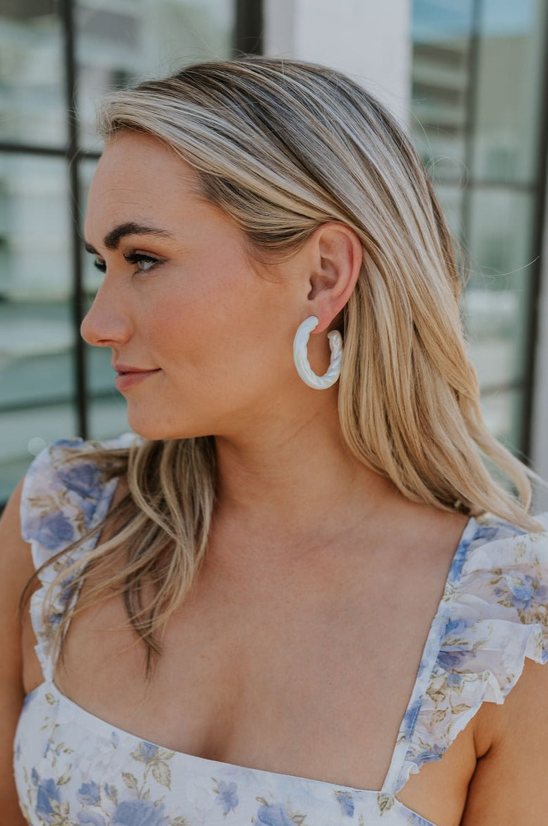 Side view of female model wearing the Myra Iridescent Hoop Earrings that have white iridescent material.