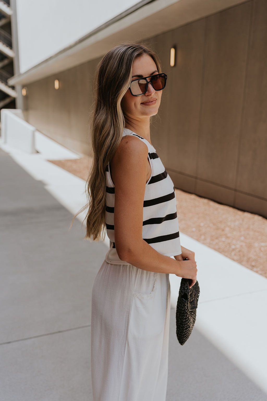 side view of female model wearing the Mallory Off White & Black Stripe Tank which features White and Black Stripe Pattern, Round Neckline, Cropped Waist and Sleeveless