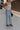 side view of female model wearing the Charli Cropped Wide Leg Pants which features Denim-Like Fabric, Wide Pant Legs, Raw Hem, Monochrome Front Button with Zipper Closure, Two Front Pockets, Two Back Pockets and Belt Loops. the pants are available in blue and pink.