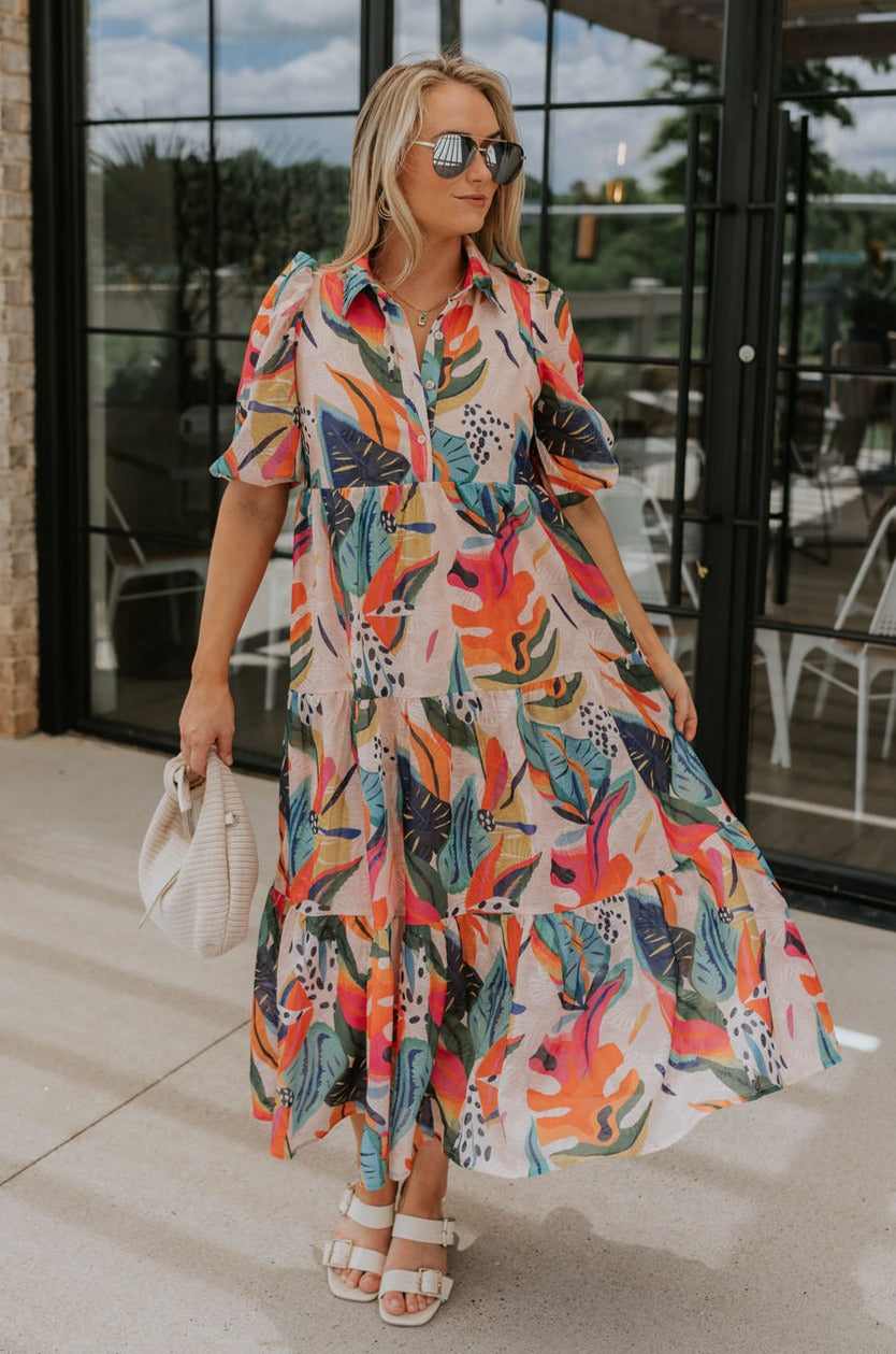 Full body view of female model wearing the Alora Multi Palm Floral Midi Dress which features Multi Color Floral Palm Print, Tan Lining, Tiered Body, Midi Length, Quarter Button-Up, Collared Neckline and Short Puff Sleeves