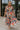 Full body view of female model wearing the Alora Multi Palm Floral Midi Dress which features Multi Color Floral Palm Print, Tan Lining, Tiered Body, Midi Length, Quarter Button-Up, Collared Neckline and Short Puff Sleeves