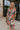 Full body view of female model wearing the Alora Multi Palm Floral Midi Dress which features Multi Color Floral Palm Print, Tan Lining, Tiered Body, Midi Length, Quarter Button-Up, Collared Neckline and Short Puff Sleeves