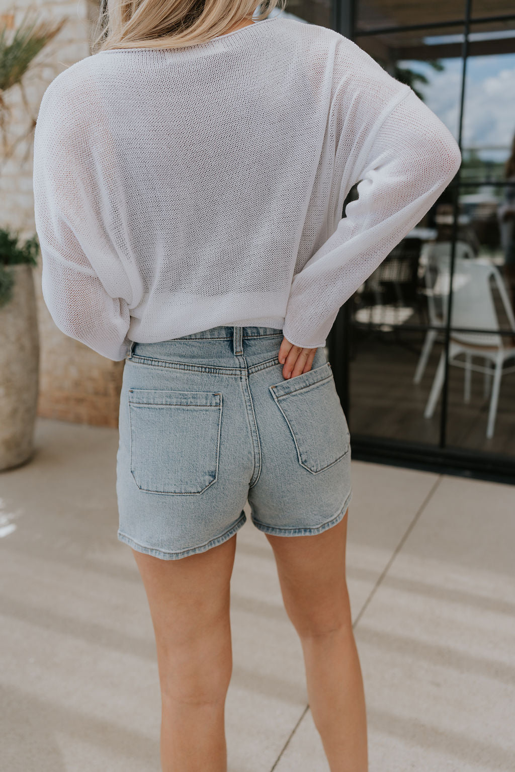 back view of female model wearing the Alyssa Light Wash Denim Shorts which features Stretchy light denim, Front & back pockets and Front zipper & button closure