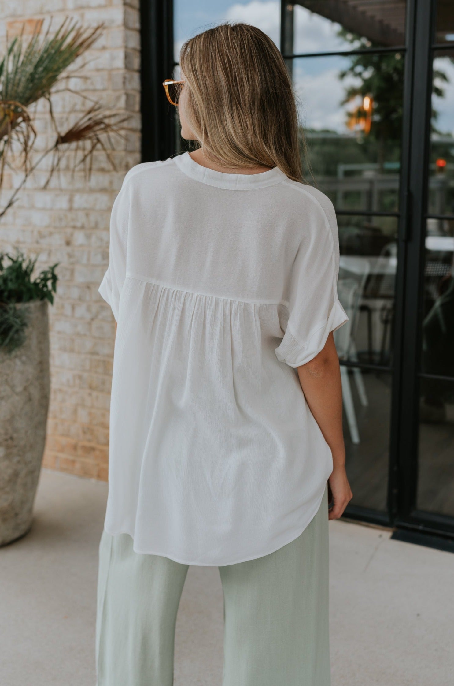 back view of female model wearing the Evie White Short Sleeve Button-Up Top which features Evie White Short Sleeve Button-Up Top