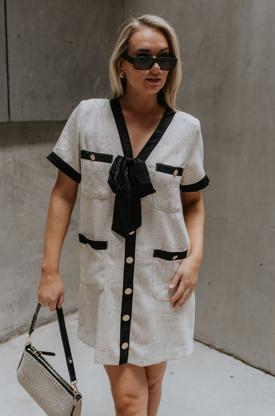 front view of female model wearing the Stevie Oatmeal & Black Short Sleeve Mini Dress which features Oatmeal Fabric, Black Trim Details, Mini Length, Anchor Button Up Detail, Four Buttoned Front Pockets, Black Tie Detail and Short Sleeves