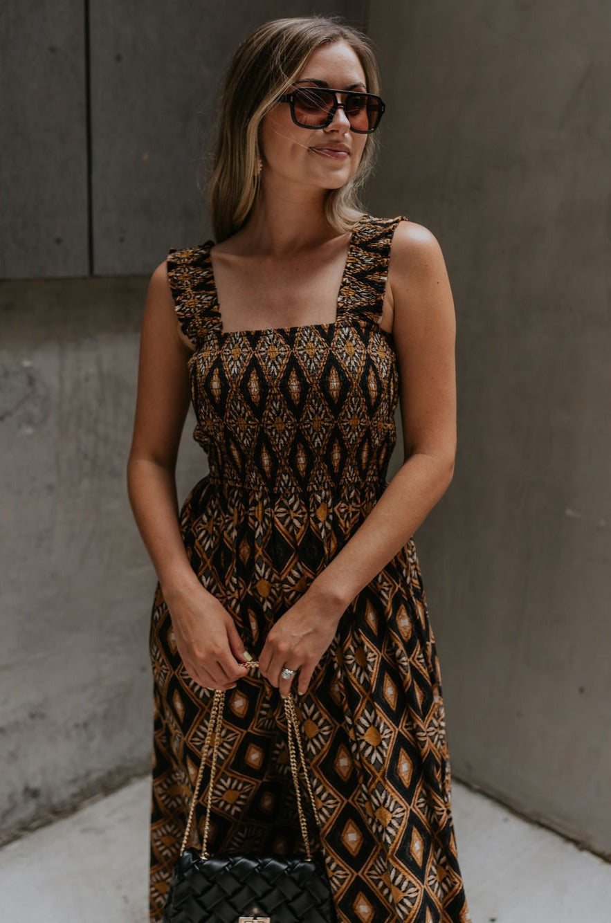 front view of female model wearing the Dahlia Black & Rust Floral Midi Dress which features Black and Rust Lightweight Fabric, Floral & Geometric Pattern, Midi Length, Smocked Upper, Thick Straps and Square Neckline