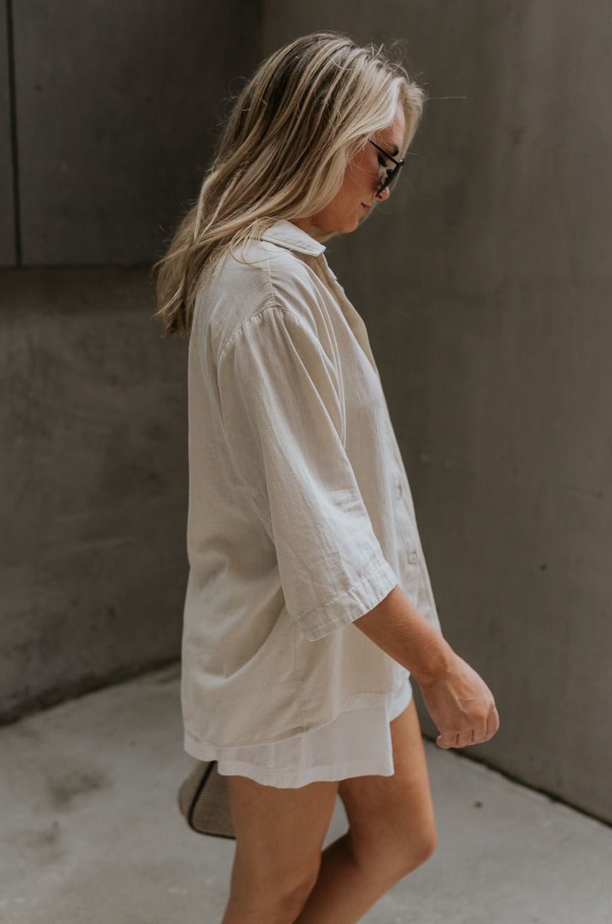 side view of female model wearing the Andrea Ecru Button-Up Top which features Ecru Cotton Fabric, Monochrome Button-Up Top, Collared Neckline, Front Left Chest Pocket and Short Sleeves