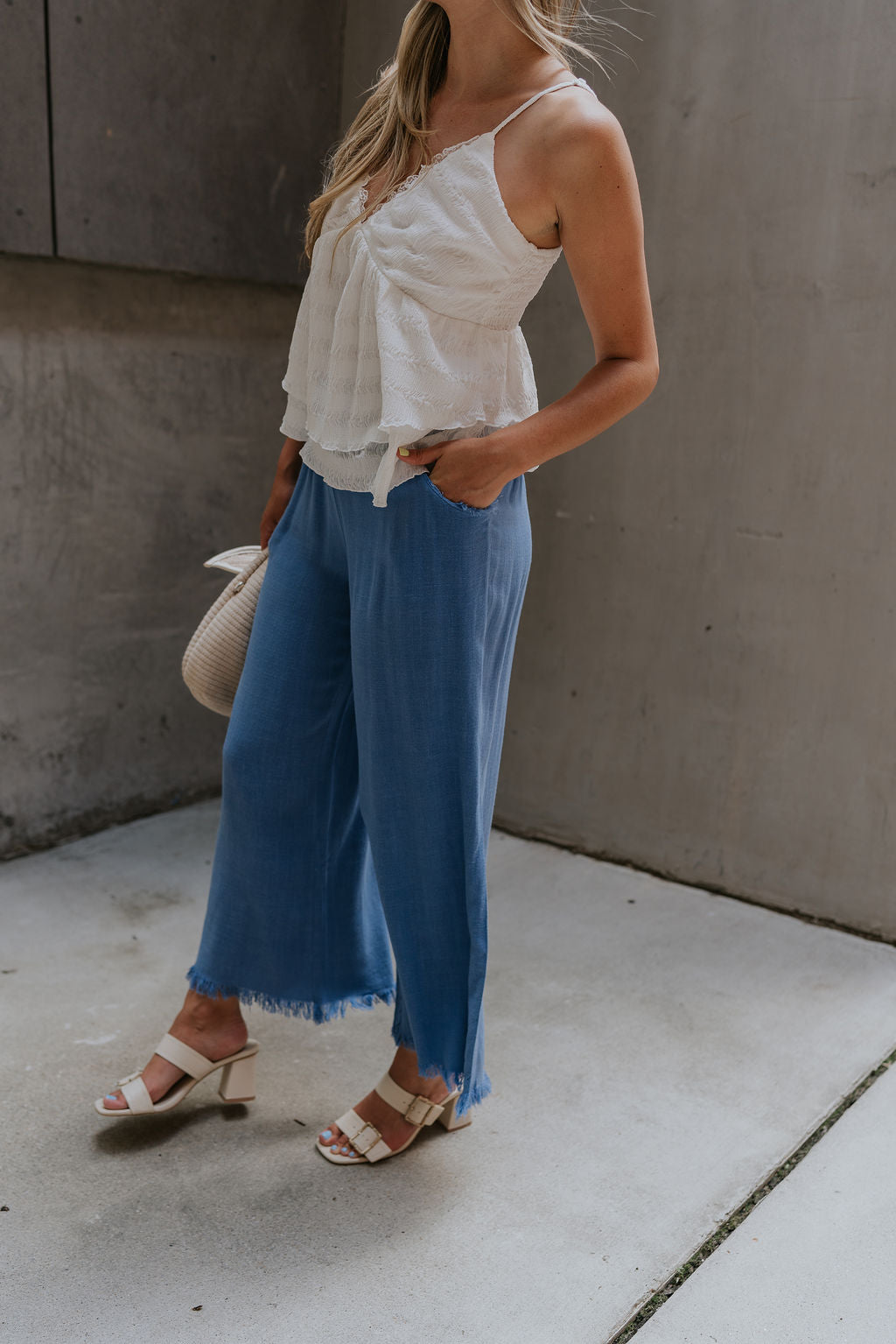 side view of female model wearing the Leona Linen Fray Cropped Pants which features Lightweight Fabric, Wide Cropped Leg, Fray Hem Details, Two Front Pockets and Elastic Waistband. the pants are available in blue, green and white.