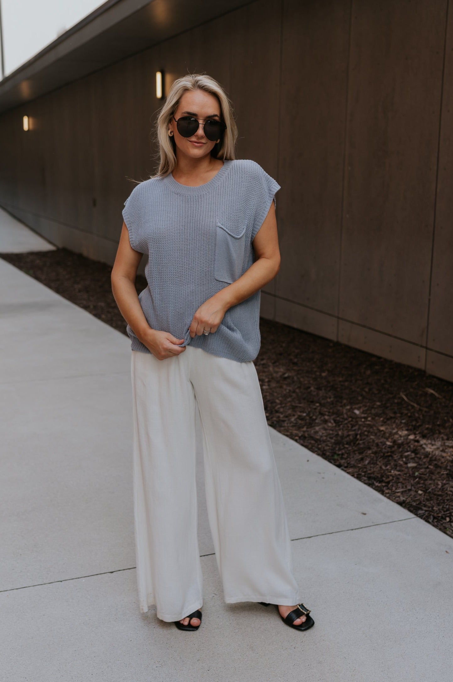 Full body front view of female model wearing the Mallorie Dusty Blue Short Sleeve Top that has light blue knit fabric, a chest pocket, and round neck. 