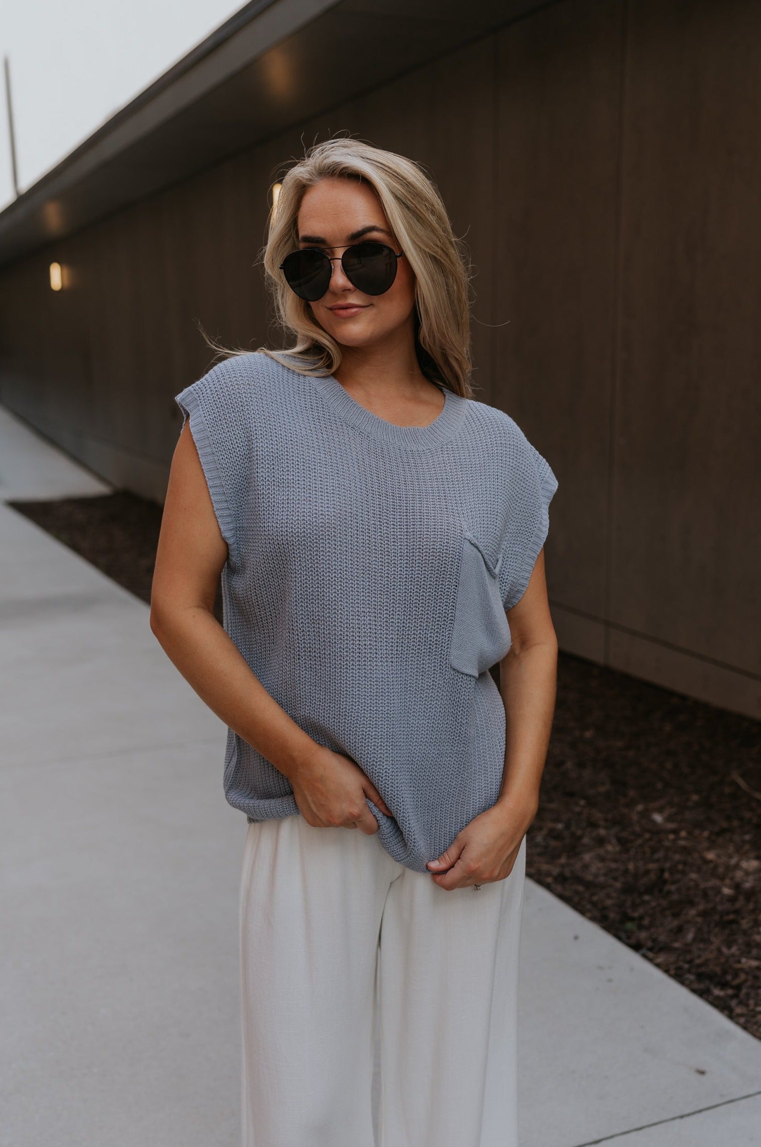 Upper body front view of female model wearing the Mallorie Dusty Blue Short Sleeve Top that has light blue knit fabric, a chest pocket, and round neck. Shown un-tucked.