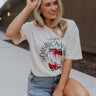 Full body view of female model wearing the It's The American Way Graphic Tee which features ream cotton fabric, round neckline, short sleeves and red, white and blue cowgirl boots graphic with "It's The American Way" writing.