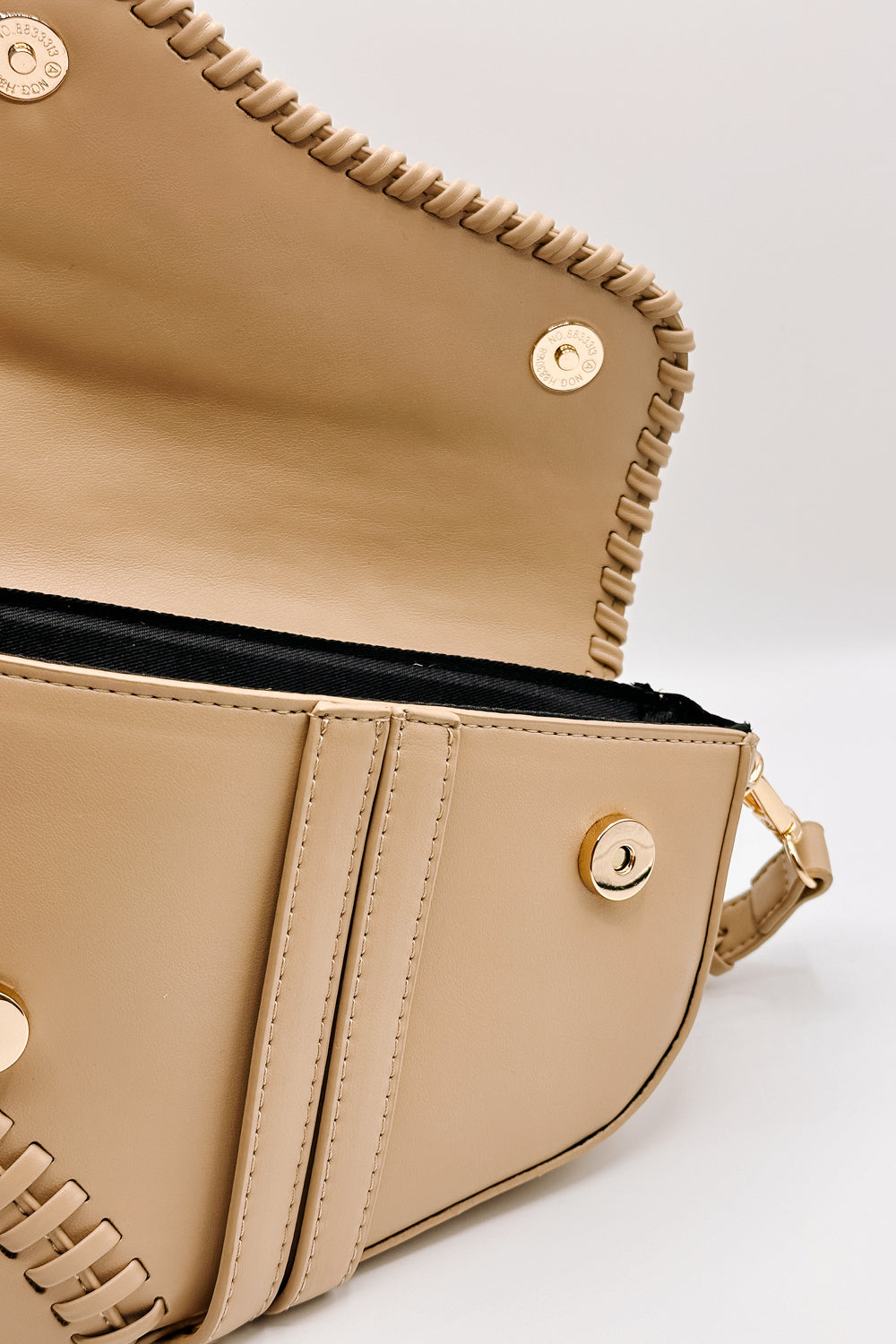 close up view of the Sloane Sand Leather Braided Strap Purse which features tan leather fabric, braided details, gold clasp closure, braided strap, tan lining and curvy hem shape