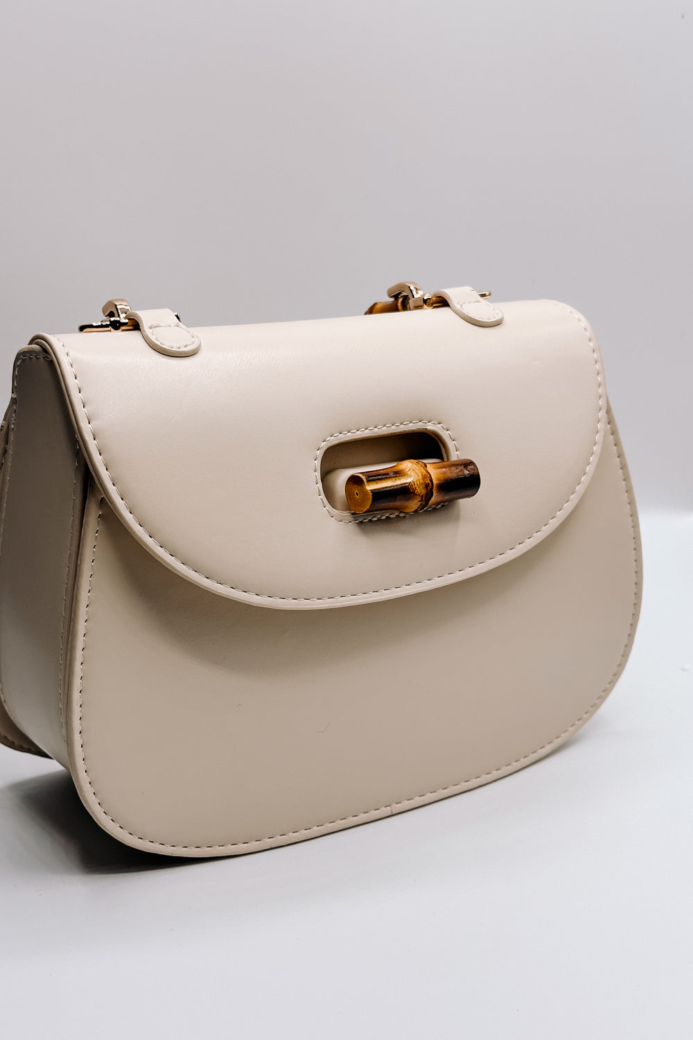 Image shows the Allison Ivory Wooden Bamboo Strap Purse which features ivory leather, wooden bamboo strap and knob closure, black lining and gold hardware details