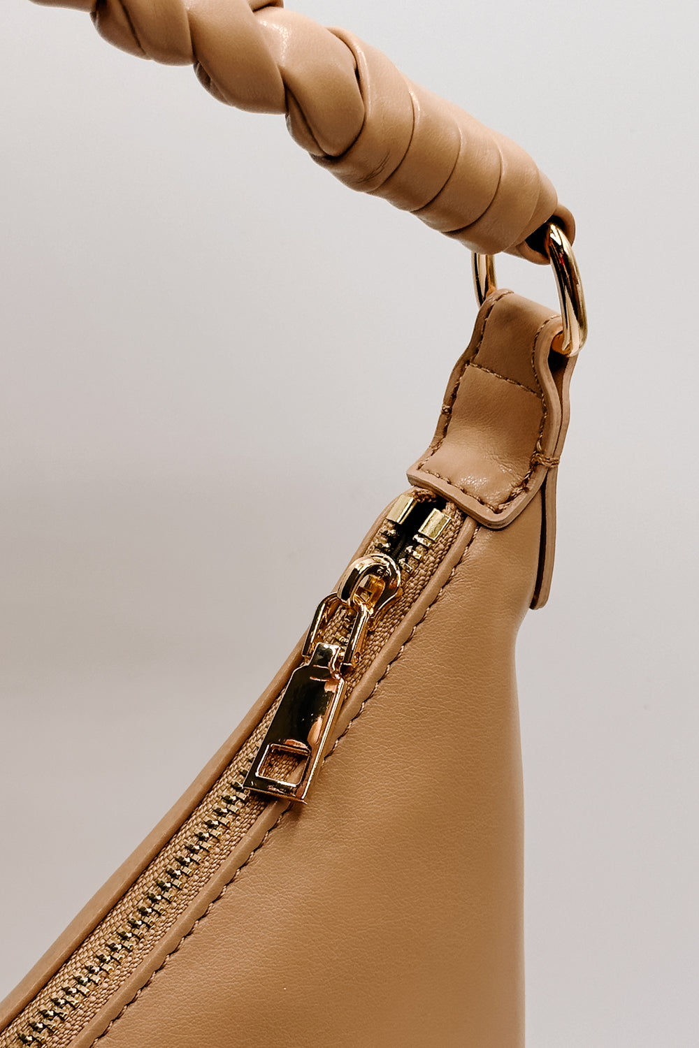 close up view of the Taylor Natural Leather Braided Strap Purse which features light brown leather fabric, gold zipper closure, gold hardware details, braided strap and herringbone lining