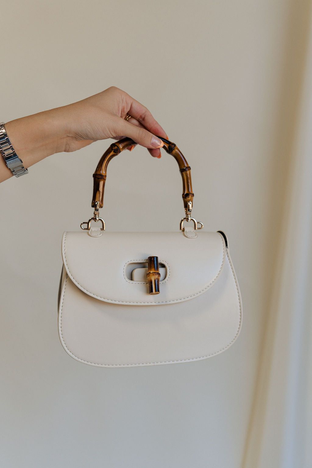 Model's hand is holding the Allison Ivory Wooden Bamboo Strap Purse which features ivory leather, wooden bamboo strap and knob closure, black lining and gold hardware details