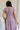 back view of female model wearing the Ellie Dusty Purple Floral Midi Dress which features Dusty Mauve Lightweight Fabric, Dusty Mauve Lining, Floral Print, Midi Length, Elastic Waistband, V Neckline and Short Sleeves