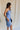 side view of female model wearing the Azlynn Blue Satin Cowl Neckline Dress which features Blue Satin Fabric, Overlay Hem Detail, Ruched Detail, Cowl Neckline with Adjustable Straps and Side Monochrome Zipper with Hook Closure