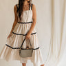 Full body view of female model wearing the Clara Ecru & Black Wavy Trim Midi Dress which features Cream Lightweight Fabric, Cream Lining, Midi Length, Pockets on each side, Black Wavy Trim Details, Square Neckline, Straps and Smocked Back