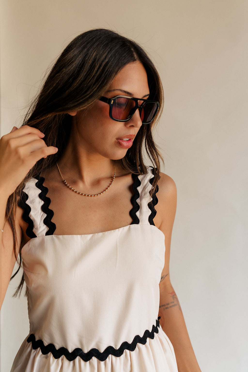 close up view of female model wearing the Clara Ecru & Black Wavy Trim Midi Dress which features Cream Lightweight Fabric, Cream Lining, Midi Length, Pockets on each side, Black Wavy Trim Details, Square Neckline, Straps and Smocked Back