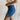 side view of female model wearing the Mylah Denim Slit Bow Mini Skirt which features Medium Denim Fabric, Mini Length, Slit Detail with Bow and Side Monochrome Zipper with Hook Closure