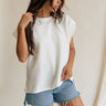 Side view of female model wearing the Blaire Off White Ribbed Short Sleeve Top which features Off White Ribbed Fabric, Round Neckline, Short Sleeves and Monochrome Button-Up Back Closure