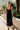 Full body back view of female model wearing the Mila Black Knit Cut-Out Trim Midi Dress which features Black Knit Fabric, Square Neckline, Straps and Cutout Details