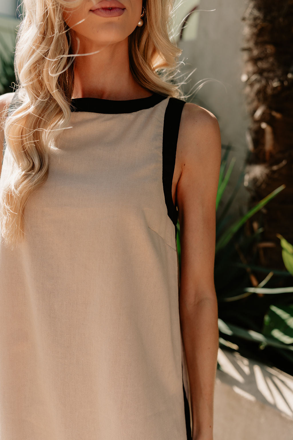 close up view of female model wearing the Camila Oatmeal & Black Sleeveless Mini Dress which features Tan Linen Fabric, Black Trim Details,Tan Lining, Mini Length, Round Neckline, Sleeveless and Monochrome Back Zipper with Hook Closure