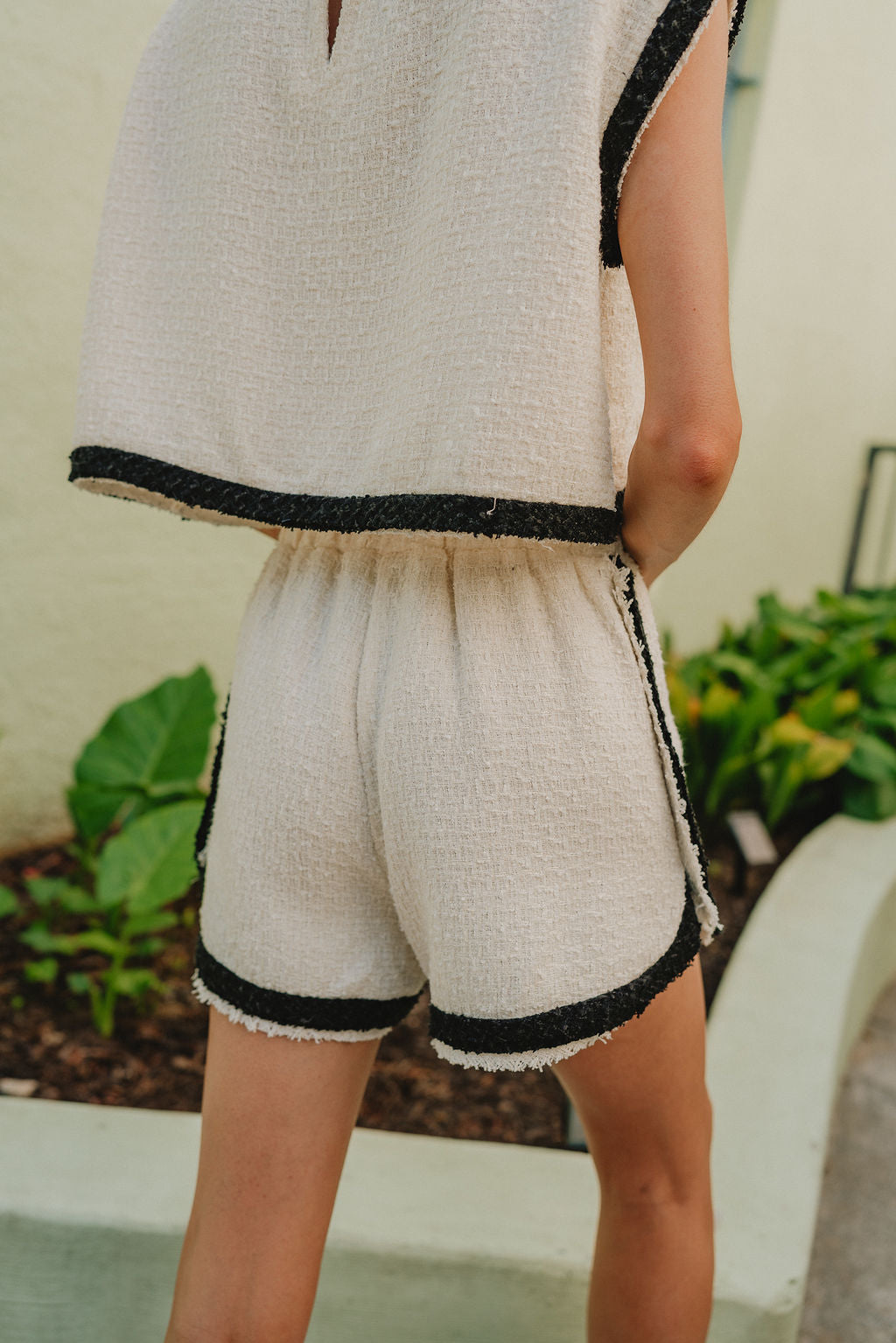 back view of female model wearing the Emery Cream & Black Shorts which features Cream Textured Fabric, Black Trim Details and Elastic Waistband with Drawstring Ties