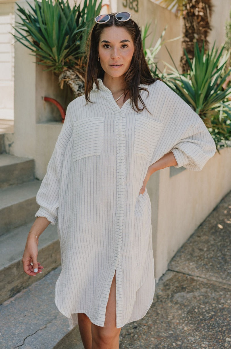 front view of female model wearing the Abigail Off White & Blue Stripe Button-Up Dress which features Off White Fabric with Thin Navy Blue Stripe Design, Midi Length/ Slit Details, Monochrome Button-Up, Two Front Chest Pockets, Collared Neckline and Long Sleeves with Buttoned Cuffs