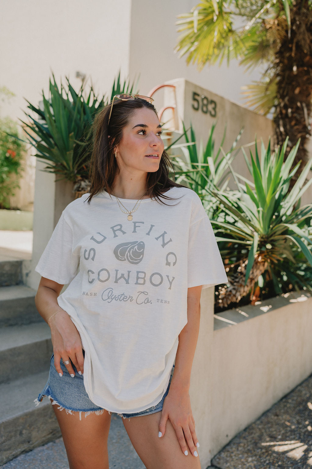 Close up front view of Surfing Cowboy Tee that says "Surfing Cowboy" and "NASH Oyster Co. TENN" with an oyster on the front, writing in grey, cream tee.