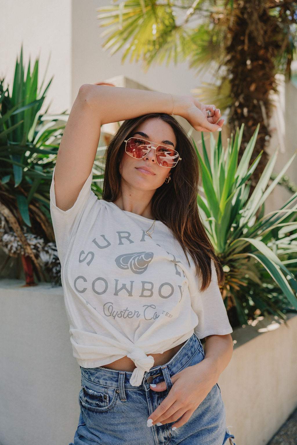 Close up front view (top tied in front) of Surfing Cowboy Tee that says "Surfing Cowboy" and "NASH Oyster Co. TENN" with an oyster on the front, writing in grey, cream tee. 