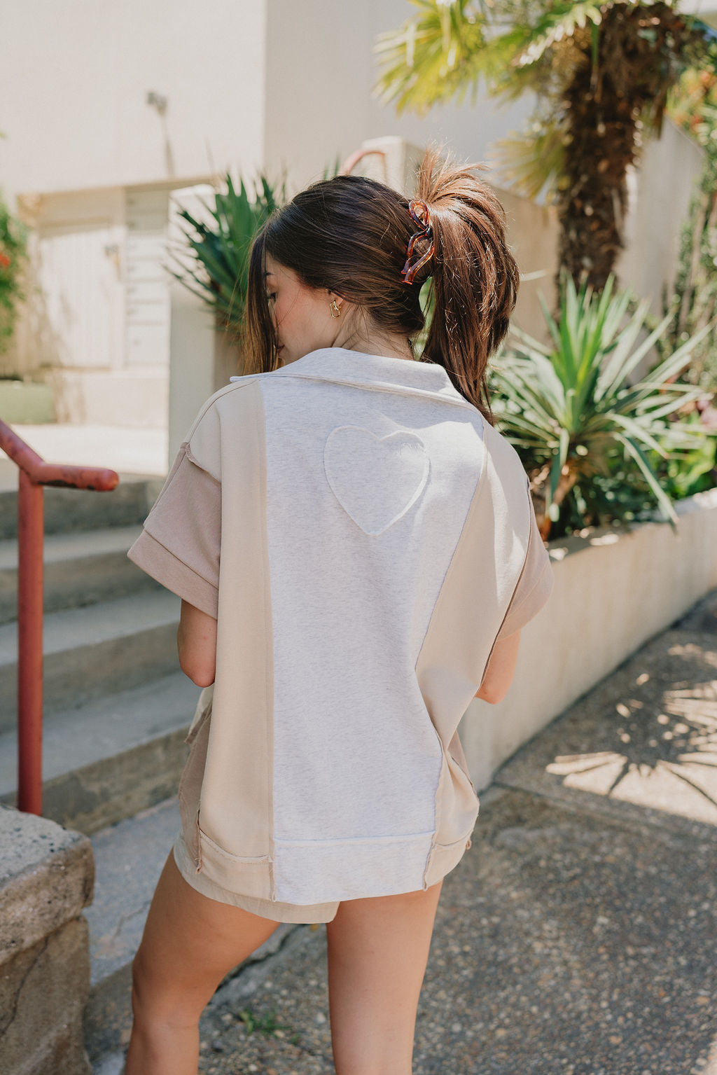 Back view of Malia Multi-Color Short Sleeve Top that is taupe, mocha, and grey, with a V and collared neckline, beautiful detailing of a heart on the back.