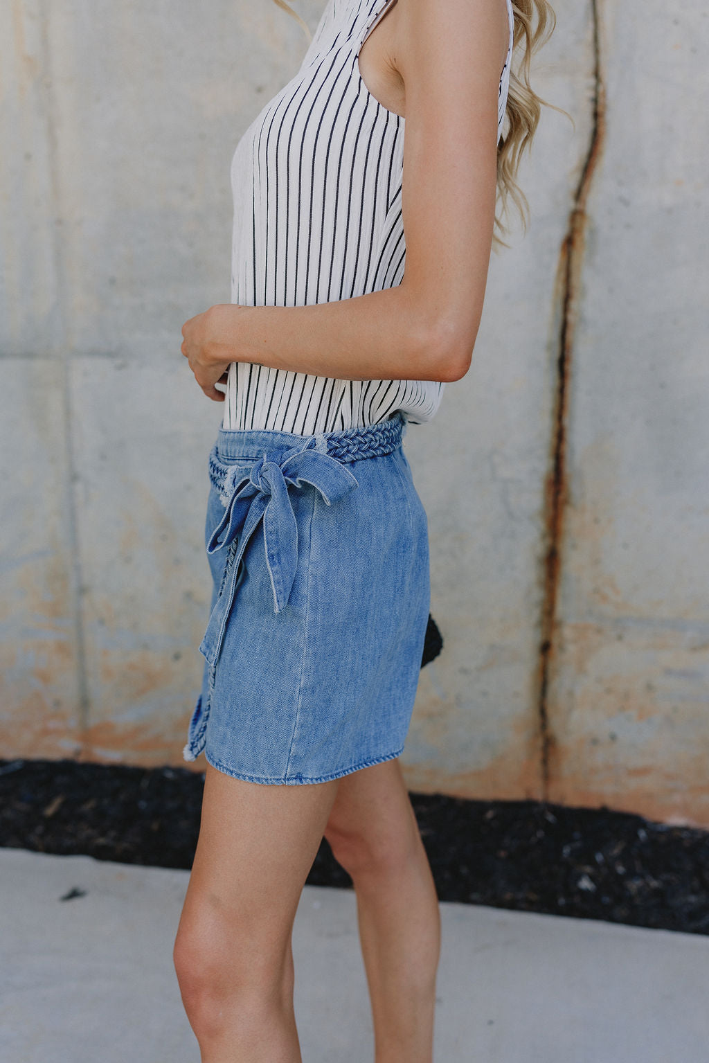 Side view of Molly Medium Wash Denim Skort that has braid details across and a cute tie on the side.