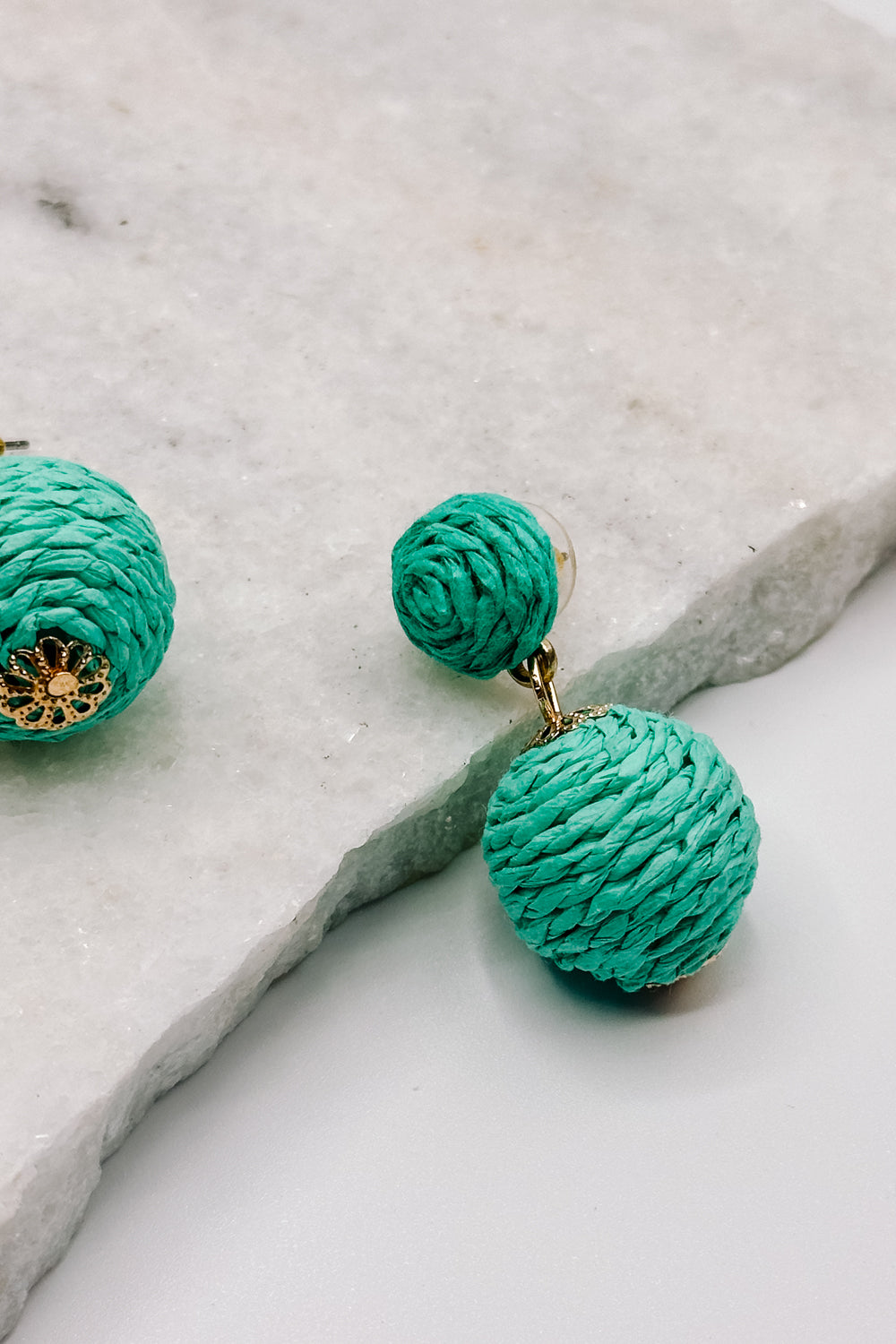 Close up view of the Sierra Green Rattan Dangle Earring which features turquoise rattan dangle ball earrings with gold details