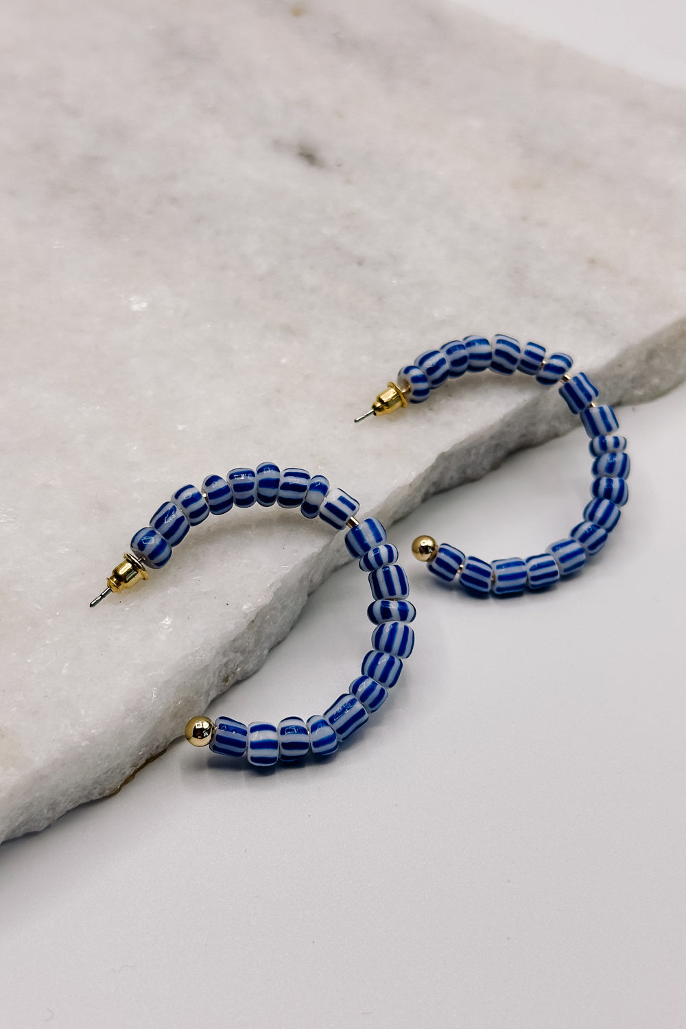 Front view of the Riley Blue & White Stripe Open Hoop Earring which features medium open hoops with blue and white stripe beads 