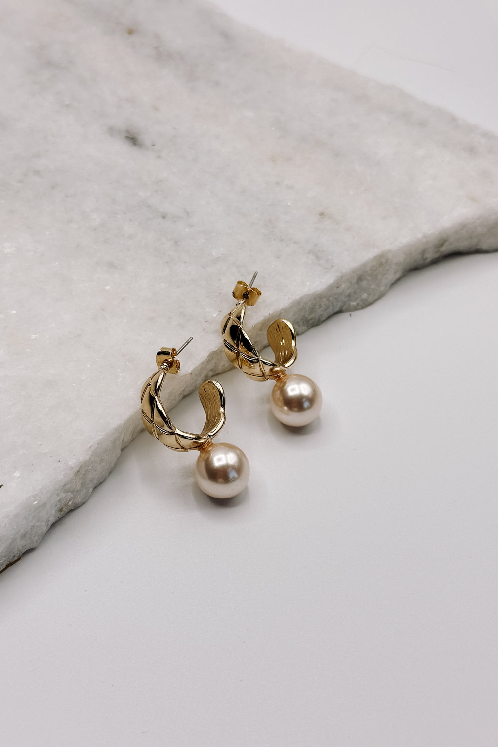 Close up view of the Skylar Pearl & Gold Hoop Dangle Earring which features gold braided mini hoops with pearl attachment