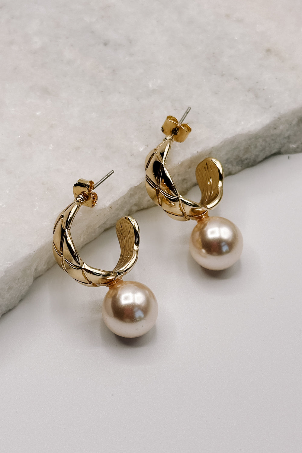 Close up view of the Skylar Pearl & Gold Hoop Dangle Earring which features gold braided mini hoops with pearl attachment