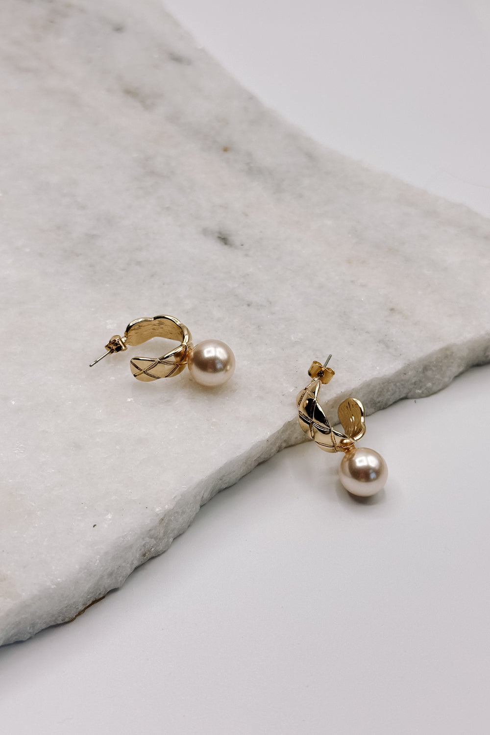 Close up view of the Skylar Pearl & Gold Hoop Dangle Earring which features gold braided mini hoops with pearl attachment