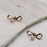 close up view of the Iris Pink & Gold Bow Stud Earring which features gold bow shaped studs with light pink pearl beads