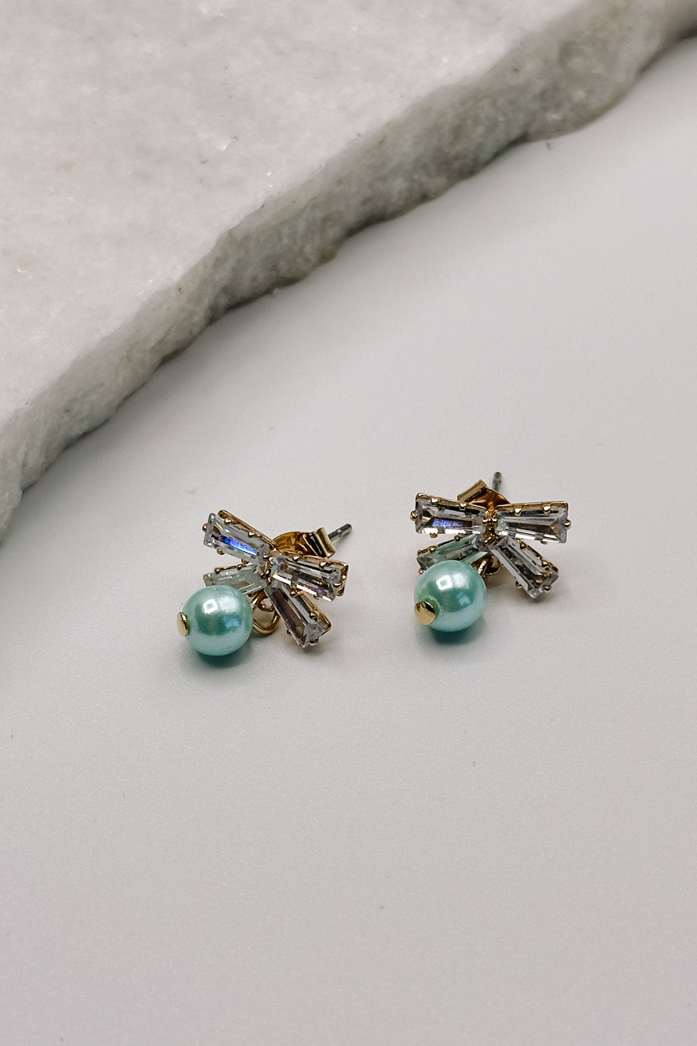 Close up view of the Talia Turquoise & Rhinestone Bow Stud Earring which features mini rhinestone bow studs with turquoise beads