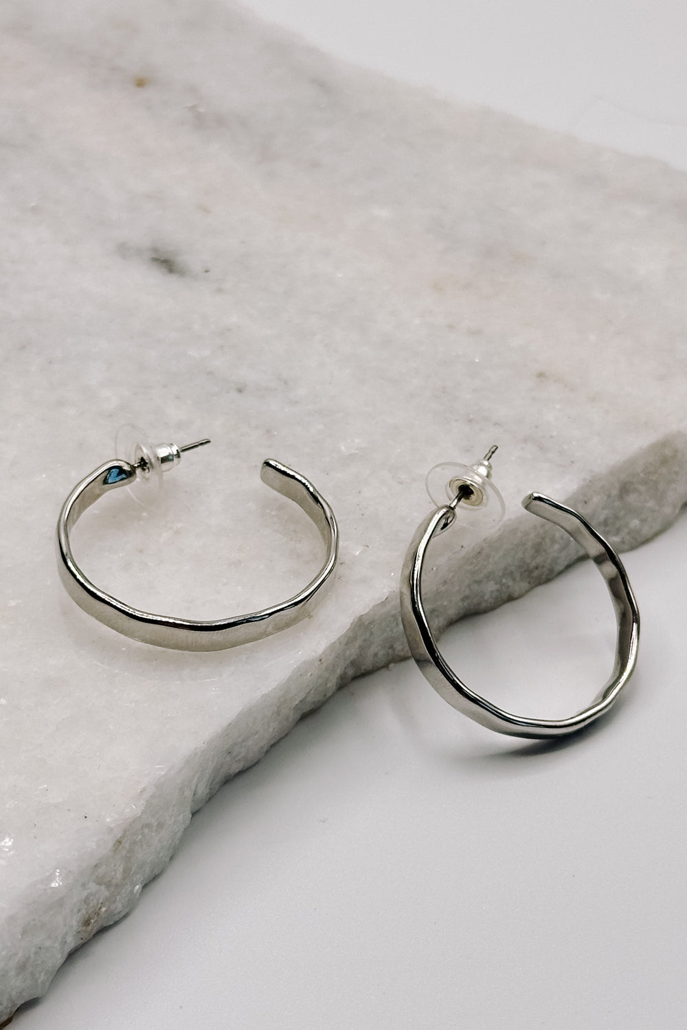 Close up view of the Layla Silver Hammered Hoop Earring which features medium open silver hammered hoops